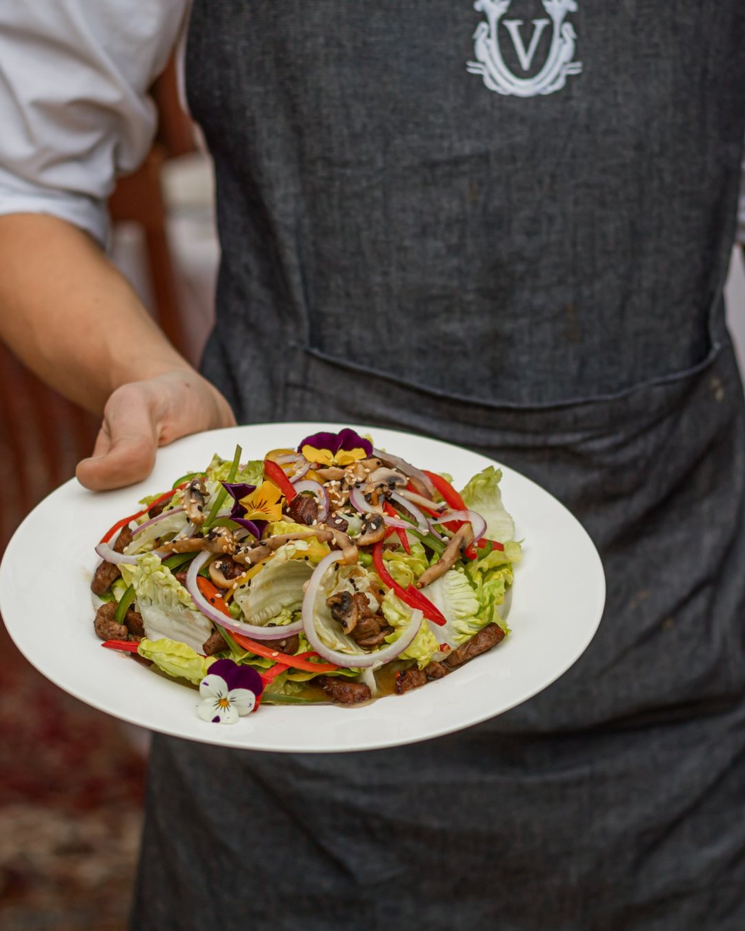 Val De Vine: a waiter in a crested apron carrying a plated salad